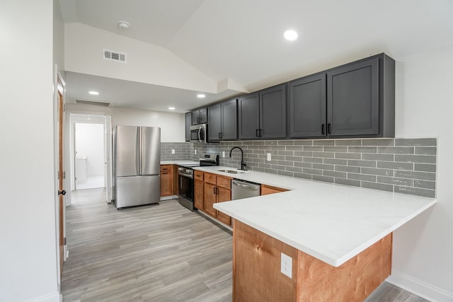 kitchen with lofted ceiling, appliances with stainless steel finishes, brown cabinetry, a sink, and a peninsula