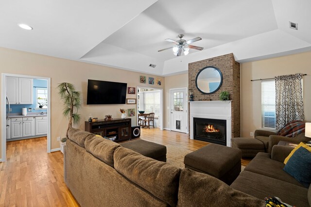 living area with light wood-type flooring, visible vents, a raised ceiling, and a fireplace