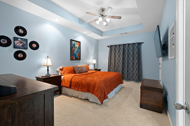 bedroom featuring visible vents, a raised ceiling, light carpet, and ceiling fan