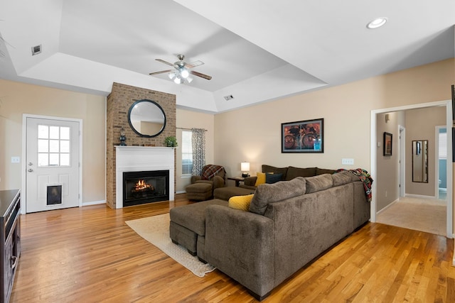 living room with plenty of natural light, a brick fireplace, light wood-style floors, and a tray ceiling