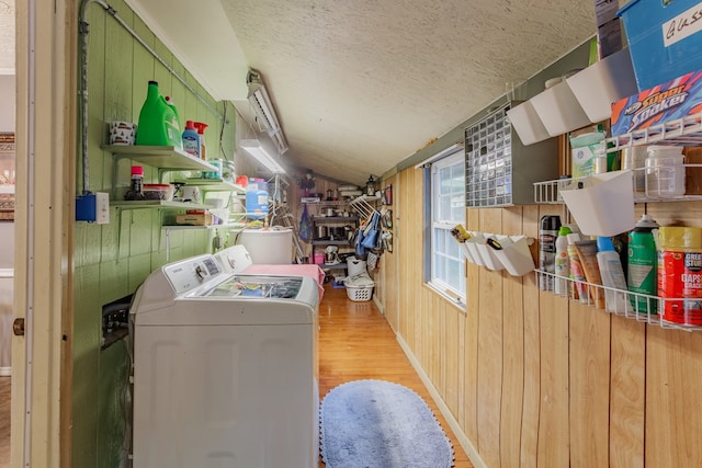 clothes washing area featuring wood walls, laundry area, wood finished floors, washing machine and dryer, and a textured ceiling