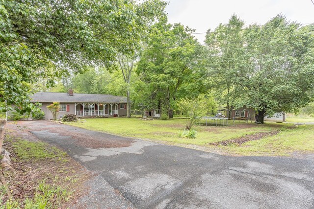 single story home with a trampoline, a chimney, driveway, covered porch, and a front yard