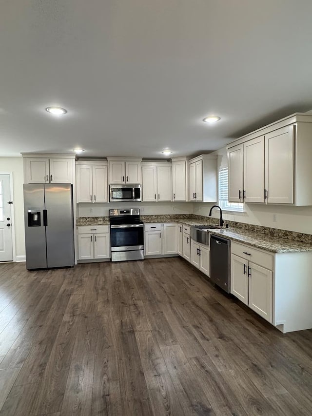 kitchen featuring light stone counters, appliances with stainless steel finishes, dark wood-type flooring, white cabinetry, and a sink