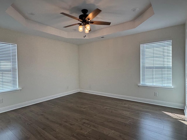 unfurnished room with dark wood-style floors, a raised ceiling, ceiling fan, and baseboards