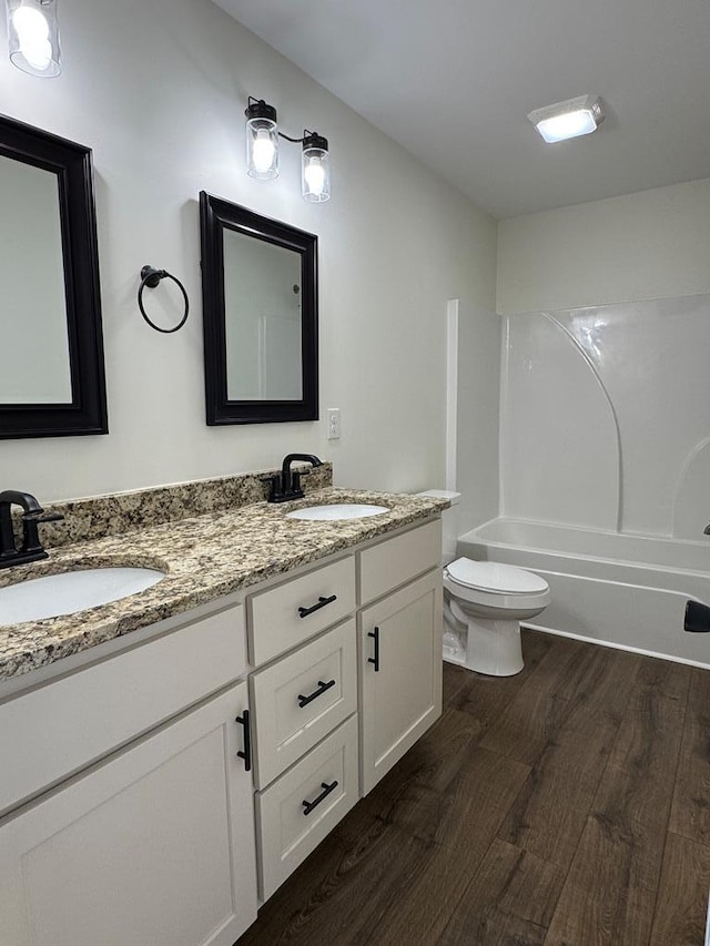 full bath featuring double vanity, a sink, toilet, and wood finished floors