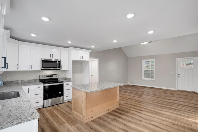 kitchen featuring stainless steel appliances, white cabinetry, a kitchen island, and light stone counters