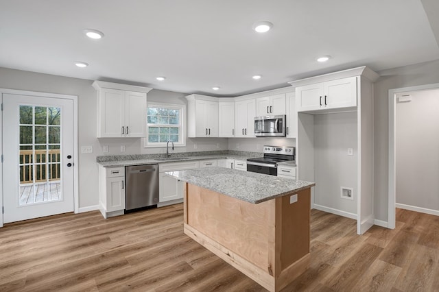 kitchen featuring a kitchen island, appliances with stainless steel finishes, white cabinetry, light stone countertops, and light wood-type flooring