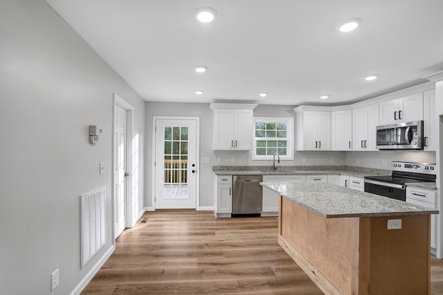 kitchen with white cabinetry, light stone counters, a center island, appliances with stainless steel finishes, and light hardwood / wood-style floors