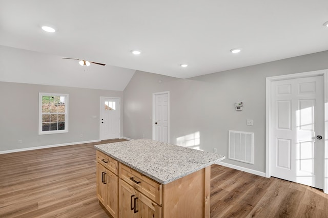 kitchen with lofted ceiling, ceiling fan, a center island, light stone counters, and light hardwood / wood-style floors