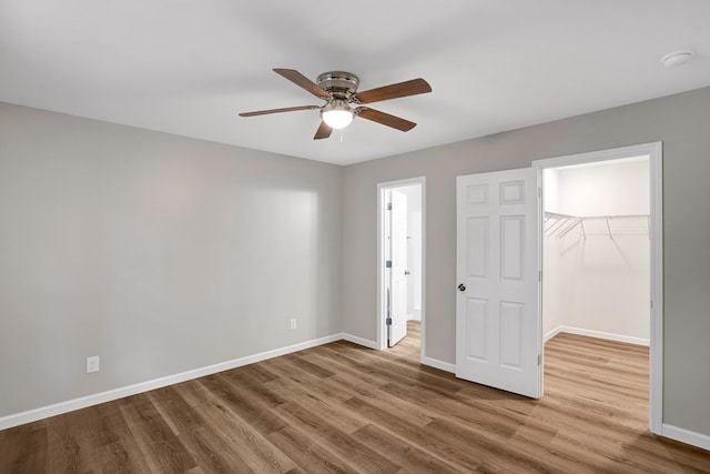 unfurnished bedroom with hardwood / wood-style flooring, a spacious closet, ceiling fan, and a closet