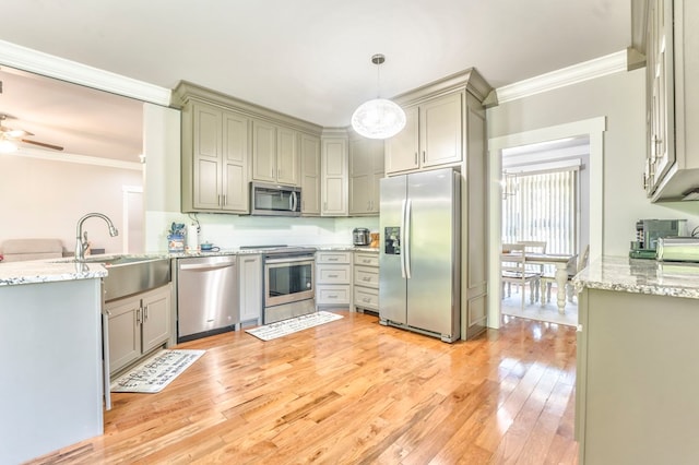 kitchen with appliances with stainless steel finishes, sink, hanging light fixtures, ornamental molding, and light wood-type flooring