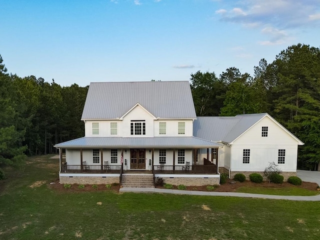 country-style home featuring a front yard, a wooded view, covered porch, and metal roof