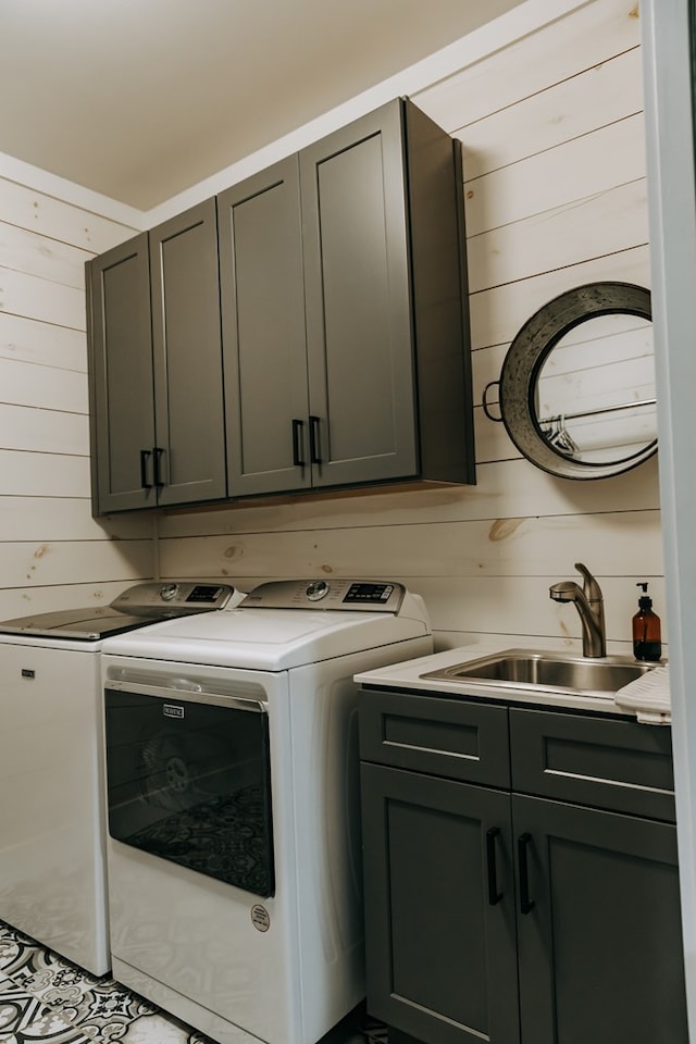 laundry area with wood walls, separate washer and dryer, cabinet space, and a sink
