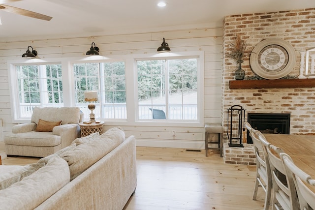living room featuring ceiling fan, wooden walls, light wood-style flooring, and a brick fireplace