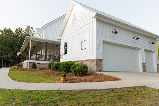 view of side of home with concrete driveway, board and batten siding, brick siding, and covered porch