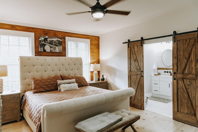 bedroom with multiple windows, connected bathroom, a barn door, and ceiling fan