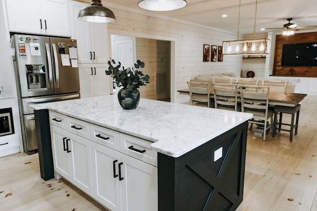 kitchen with light stone counters, light wood finished floors, stainless steel fridge, a kitchen island, and white cabinets