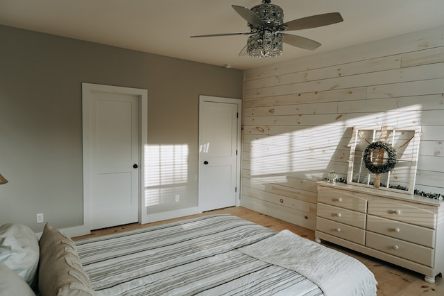 bedroom featuring light wood-style floors, wooden walls, and a ceiling fan