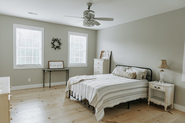 bedroom featuring light wood-style floors, visible vents, baseboards, and ceiling fan