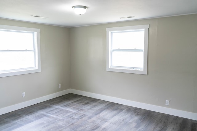 empty room with wood finished floors, visible vents, and baseboards