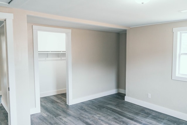 unfurnished bedroom with a closet, baseboards, dark wood-type flooring, and a spacious closet