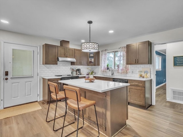 kitchen with a sink, under cabinet range hood, a kitchen bar, light wood-style floors, and recessed lighting