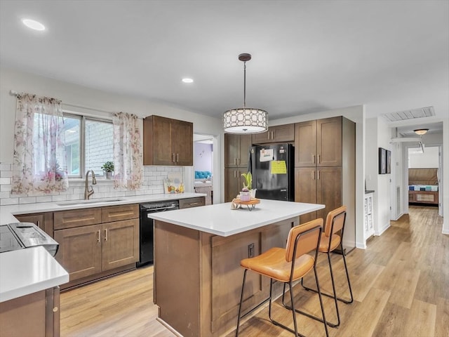kitchen with black appliances, a sink, a kitchen island, light wood finished floors, and tasteful backsplash