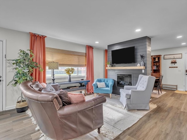 living area featuring wood finished floors, a large fireplace, recessed lighting, and baseboards