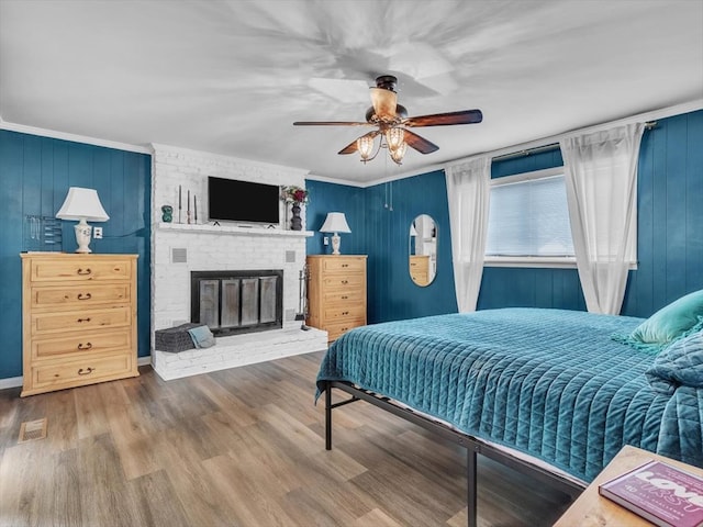 bedroom featuring wood finished floors, a brick fireplace, ornamental molding, and a ceiling fan