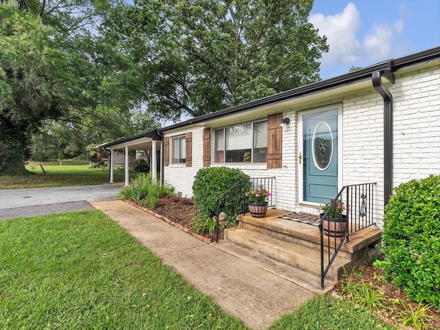 view of front of property featuring brick siding, driveway, a front lawn, and a carport