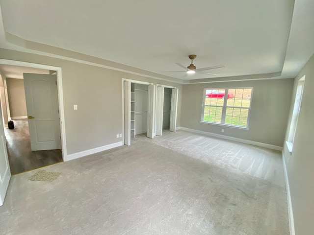 unfurnished bedroom with multiple closets, light colored carpet, and ceiling fan