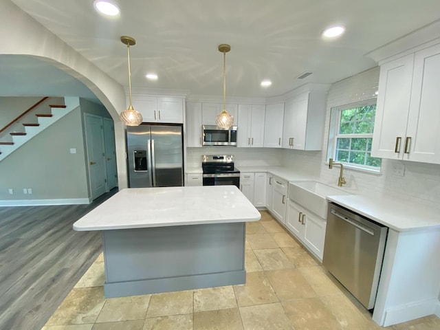 kitchen with stainless steel appliances, a kitchen island, hanging light fixtures, and white cabinets