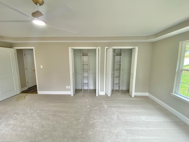 unfurnished bedroom featuring ceiling fan, light carpet, and two closets