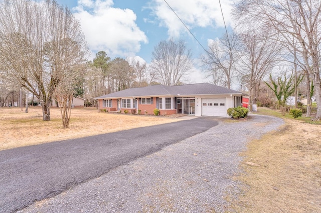 single story home with gravel driveway, brick siding, and a garage