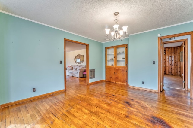 empty room with a notable chandelier, a textured ceiling, light wood-type flooring, and baseboards