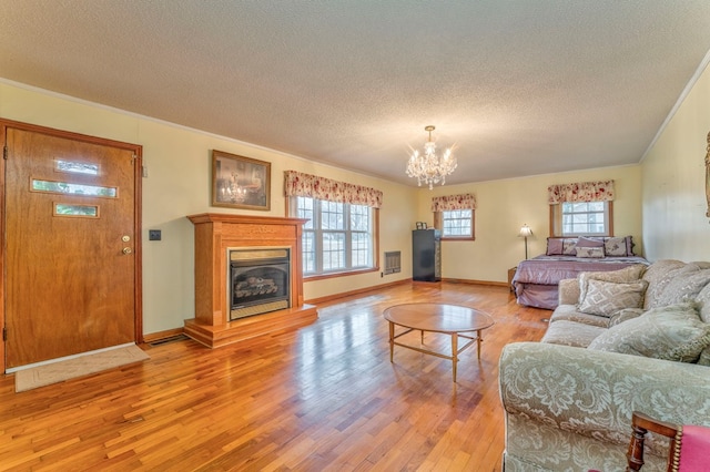 living room featuring light wood-type flooring, a healthy amount of sunlight, a glass covered fireplace, and a chandelier