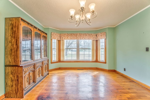 unfurnished dining area with an inviting chandelier, crown molding, light wood-style floors, and baseboards