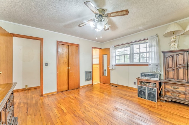 unfurnished bedroom with heating unit, baseboards, ornamental molding, light wood-style floors, and a textured ceiling