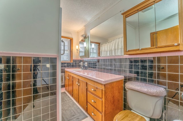 bathroom featuring toilet, ornamental molding, a textured ceiling, tile walls, and wainscoting