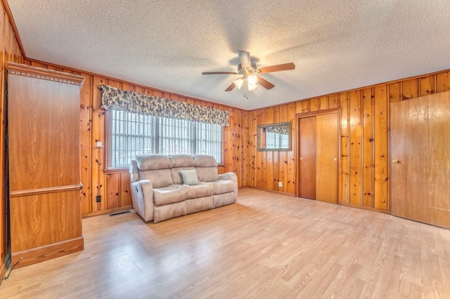 living area with a ceiling fan, wood finished floors, wood walls, and a textured ceiling