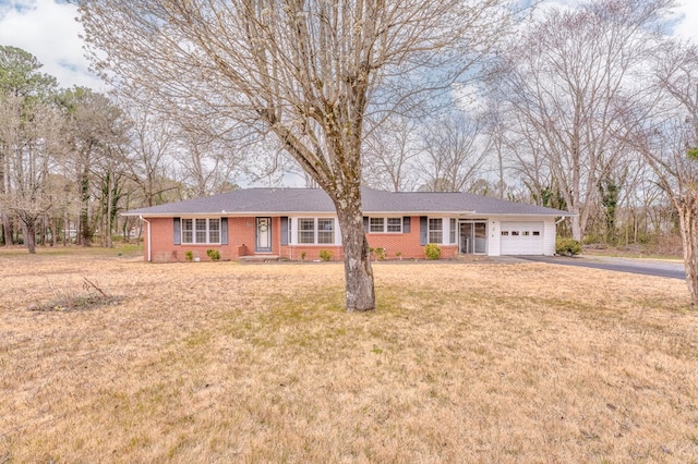 single story home with a garage, a front lawn, brick siding, and driveway