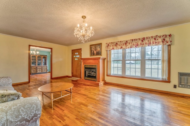 living room featuring baseboards, a chandelier, light wood-style floors, heating unit, and a glass covered fireplace