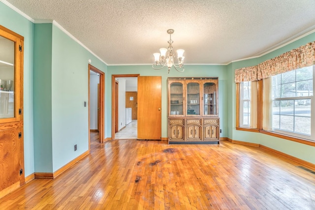 unfurnished dining area with visible vents, crown molding, light wood finished floors, baseboards, and a chandelier