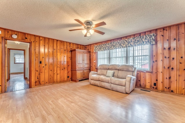 unfurnished living room featuring visible vents, light wood-style flooring, ceiling fan, wood walls, and a textured ceiling