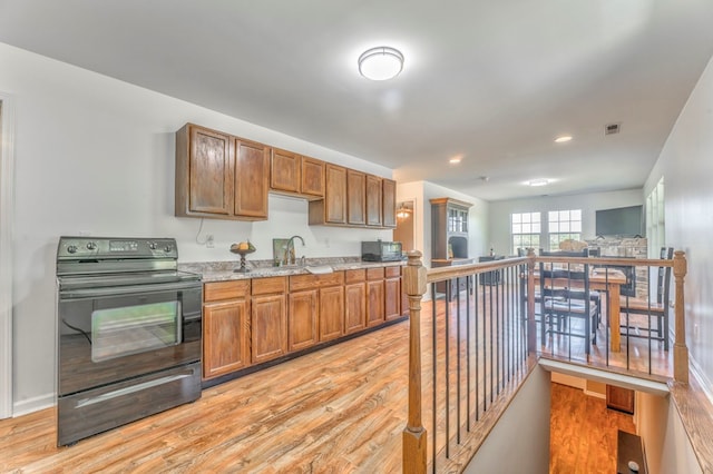 kitchen with light wood-style floors, brown cabinetry, visible vents, and black / electric stove