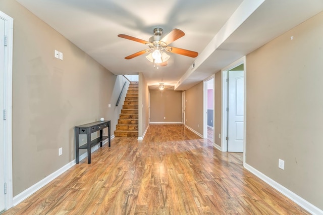 unfurnished living room with light wood-type flooring, baseboards, stairway, and ceiling fan