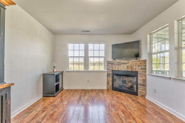 unfurnished living room featuring plenty of natural light, a stone fireplace, visible vents, and wood-type flooring