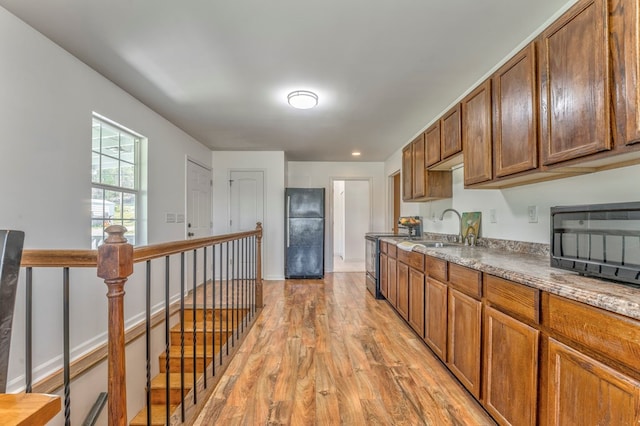 kitchen featuring brown cabinetry, light wood-style flooring, a sink, and black appliances