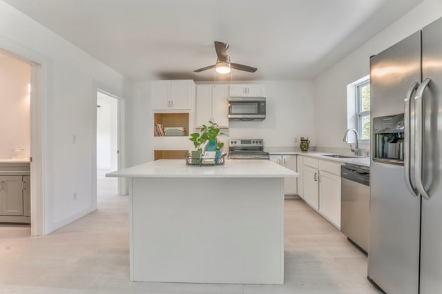 kitchen with stainless steel appliances, white cabinetry, a sink, a center island, and ceiling fan