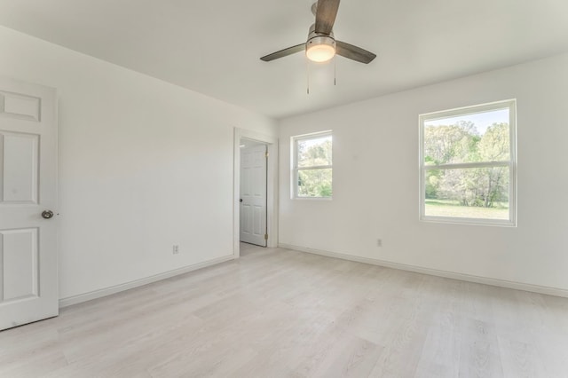 spare room with light wood finished floors, a ceiling fan, and baseboards